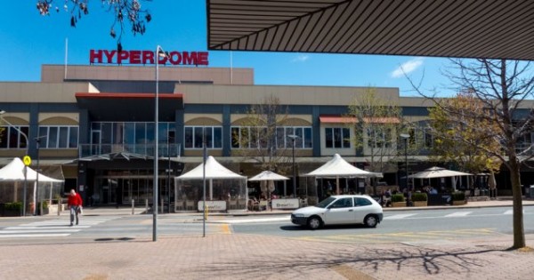 An exterior shot of the Tuggeranong Hyperdome, capturing its modern architecture and vibrant atmosphere, with shoppers bustling in and out of the various stores and eateries, illustrating the lively retail and entertainment scene in Tuggeranong.