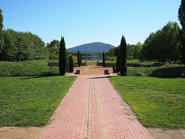 An aerial perspective of Tuggeranong Town Park, showcasing its expansive green lawns, winding pathways, and recreational facilities, with families and individuals enjoying outdoor activities amidst the natural beauty of the park.