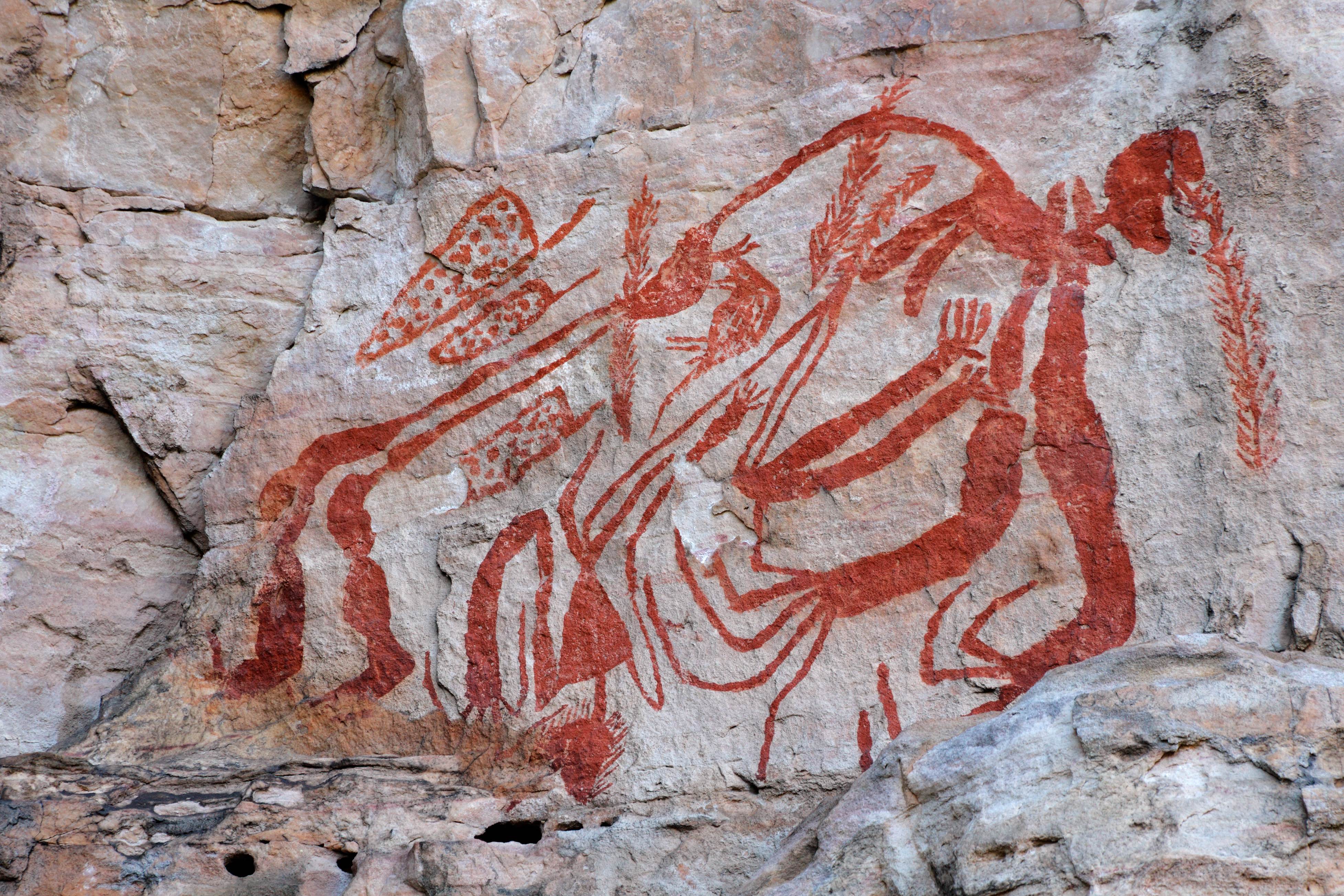 A photo of ancient rock art paintings on a sandstone rock face, depicting various symbols and figures.