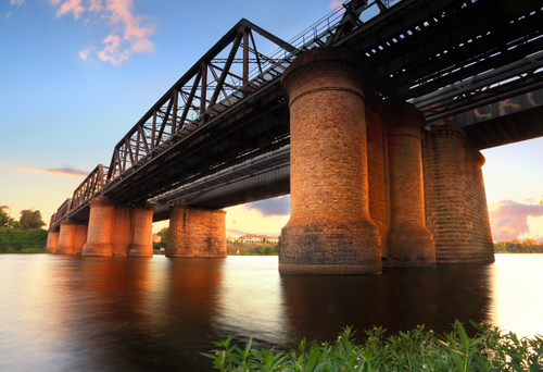 The historic Victoria Bridge illuminated in the evening, casting a warm glow over the Nepean River. This architectural marvel, with its stone piers and iron framework, stands as a testament to Penrith's rich history and progress, connecting the city's past with its present.