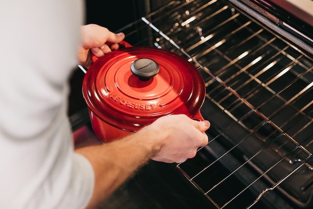 Woman putting red cast iron pot in oven