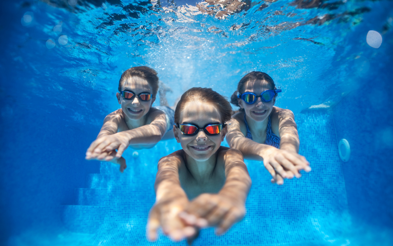 3 children diving under the water of their swimming pool as it is a heated pool so they can swim all year round