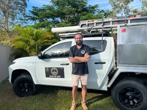 Smiling Urban Energy Electrician in branded shirt, leaning against branded ute