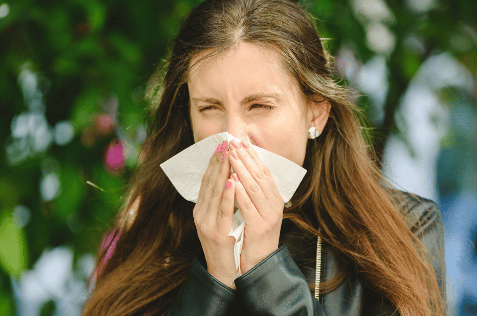 Person wiping nose with tissue stood by flowing trees