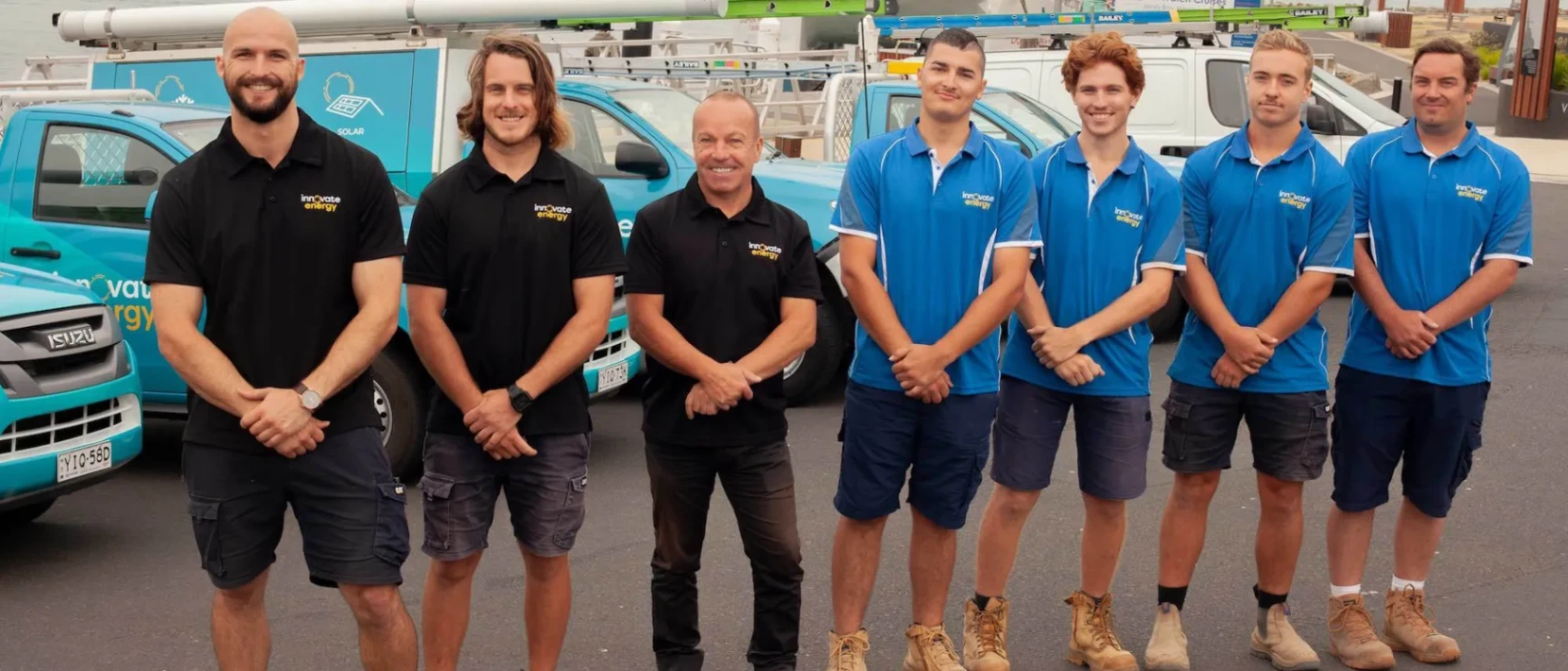 The Innovate Energy team of electricians all in branded uniform, smiling in front of branded utes