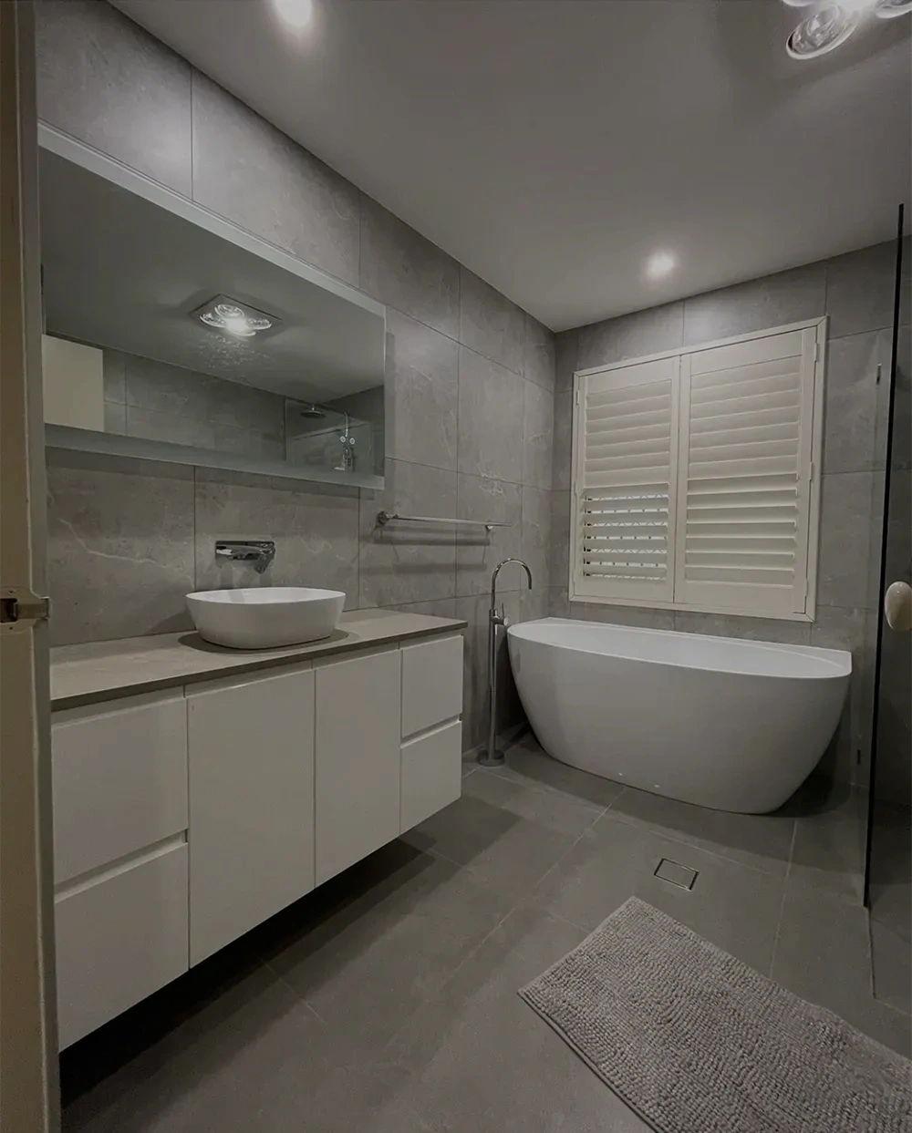 renovated bathroom, with white bathtub and sink, grey floors