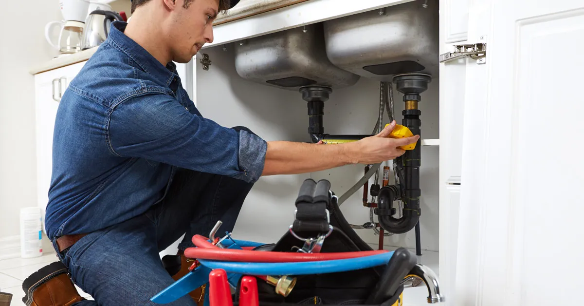 Plumber kneeling infront of a sink measuring the pipe to replace it after installing new sink and tapware