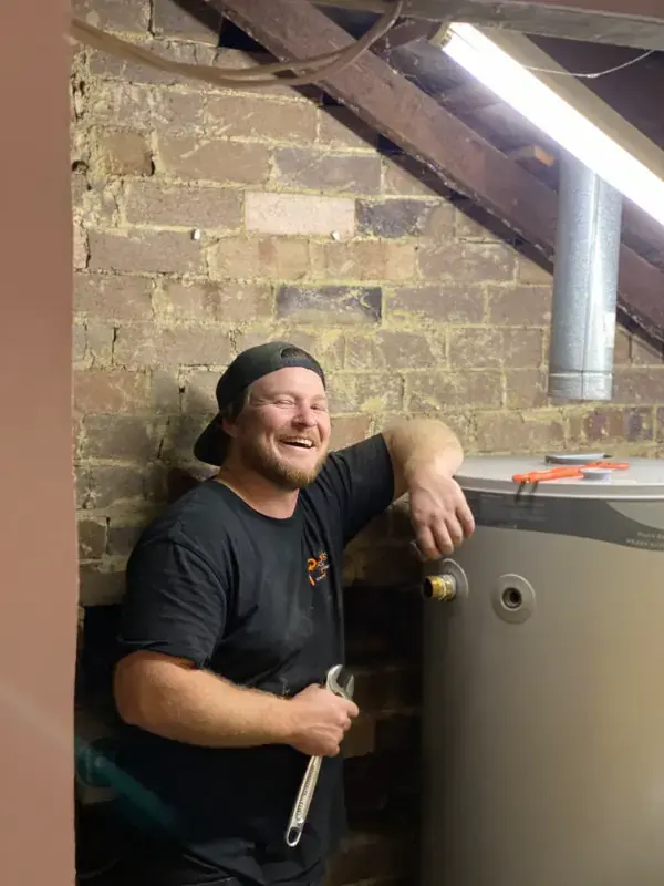 The Plumbing Professionals Hot Water Plumber Providing water heater installation, repairs and replacement services whilst smiling in The Plumbing Pros branded tshirt