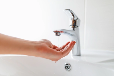 Hand being held below tap which is fully on yet only dribbling water due to low water pressure