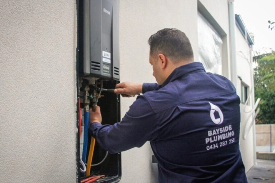 Bayside gas fitter installing Rinnai hot water system outside a commercial property. he will also complete a certificate of compliance for the new installation