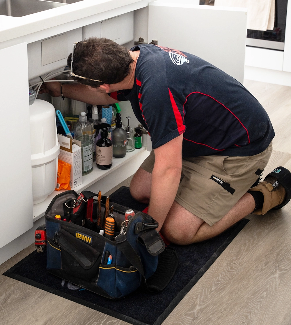 emergency plumber kneeling by sink