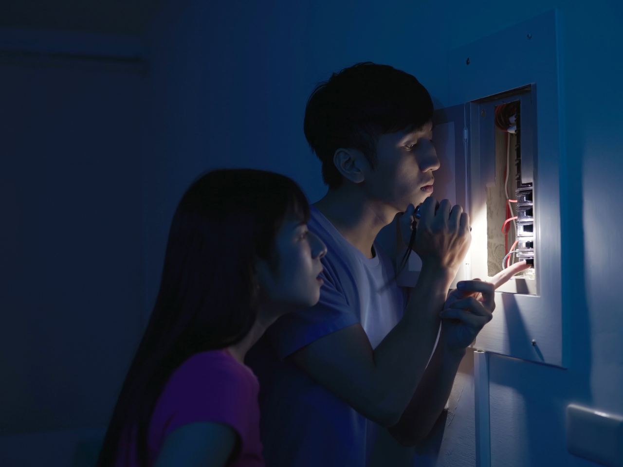 Couple in dark looking at switchboard with flashlight