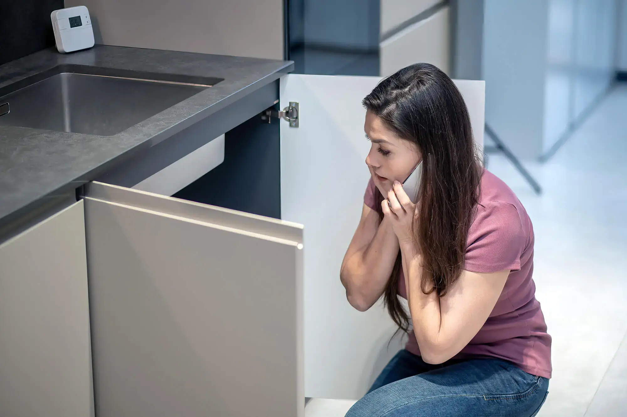 Confused lady looking under her blocked kitchen sink