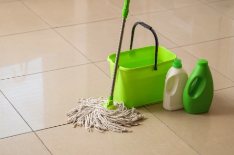 Mop, bucket and bottles of cleaning solutions on a clean and shiny bathroom tile floor
