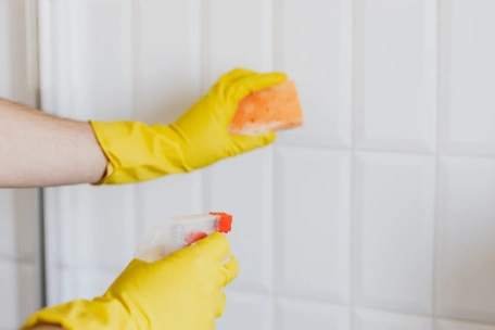 hands in rubber gloves using sponge and spray to clean bathroom tiles, which are while and look perfectly clean