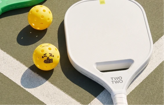 White UPCC paddle with pickleballs on court